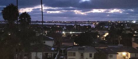 Vista nocturna de una zona residencial con casas, palmeras y un paisaje urbano distante.