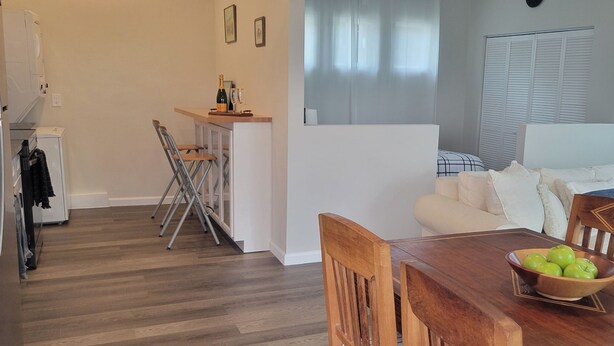 Una sala moderna con una mesa de comedor de madera, un sofá blanco y una zona de cocina con barra.