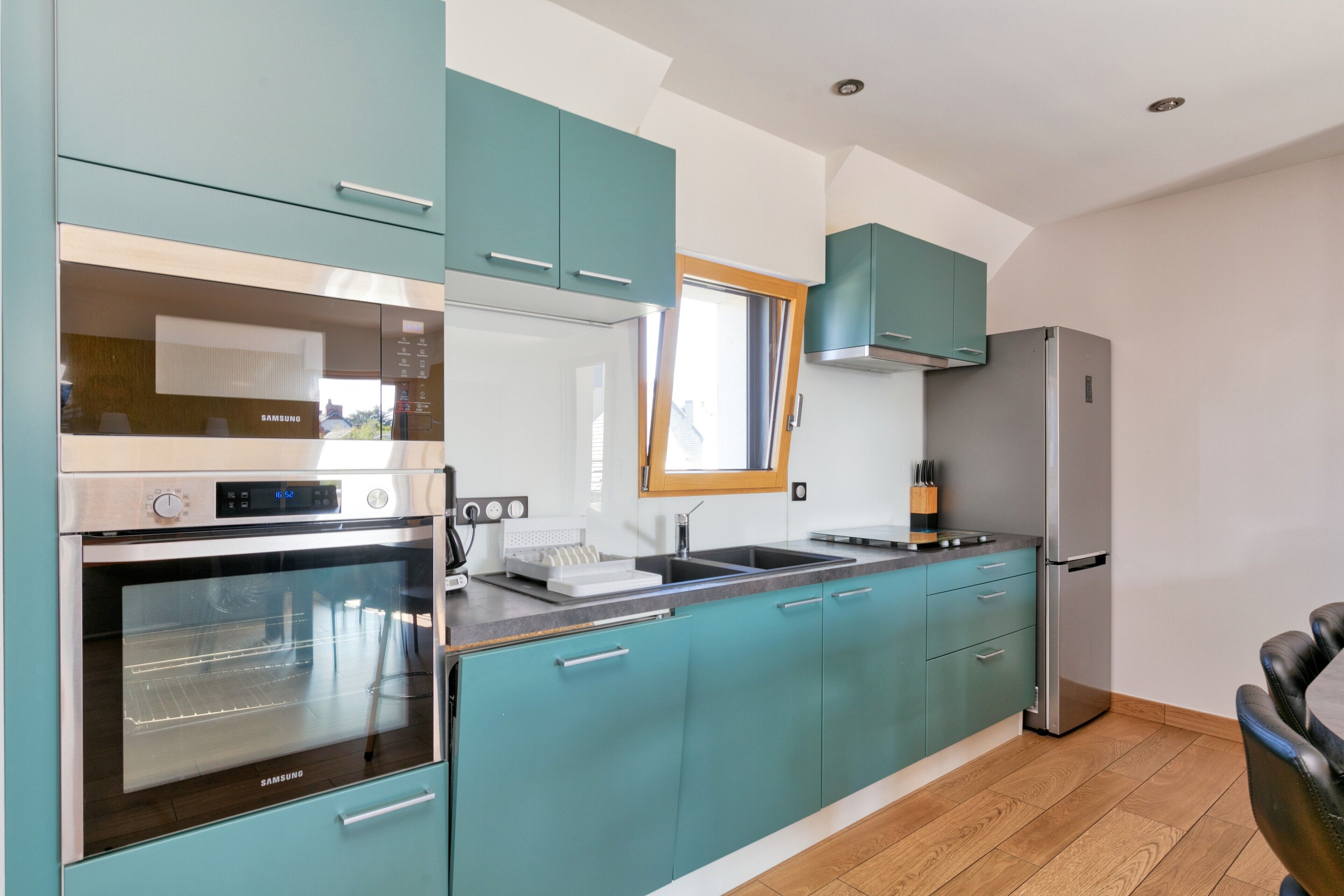 Une cuisine moderne avec des meubles de couleur turquoise, des appareils électroménagers en acier inoxydable et un plancher en bois.