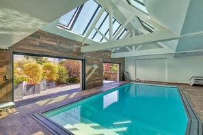 Una piscina interior moderna con tragaluces, vistas al jardín y suelo de madera.