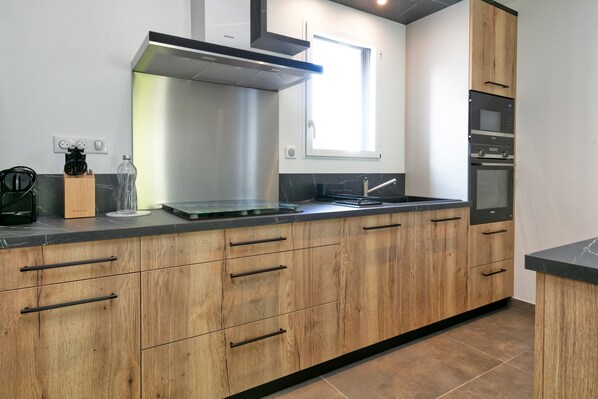 Una cocina moderna con armarios de madera, una campana extractora de acero inoxidable, un horno empotrado y un ventanal que proporciona luz natural.