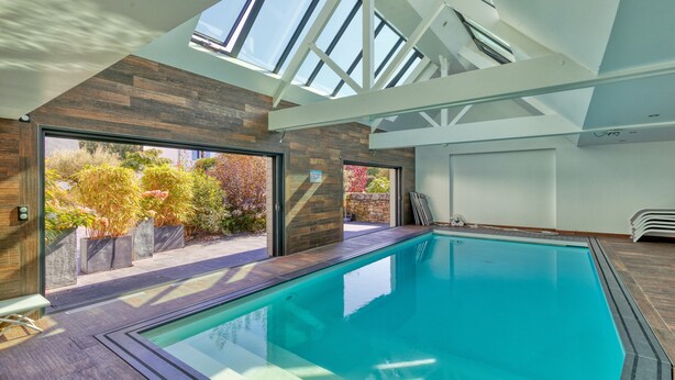A modern indoor swimming pool with skylights, a wooden floor, and a view of a garden. - Holiday Home 'Villa Ker Minet - Maison 8 Pers' with Private Terrace, Wi-Fi and Air Conditioning (Piriac-sur-Mer)