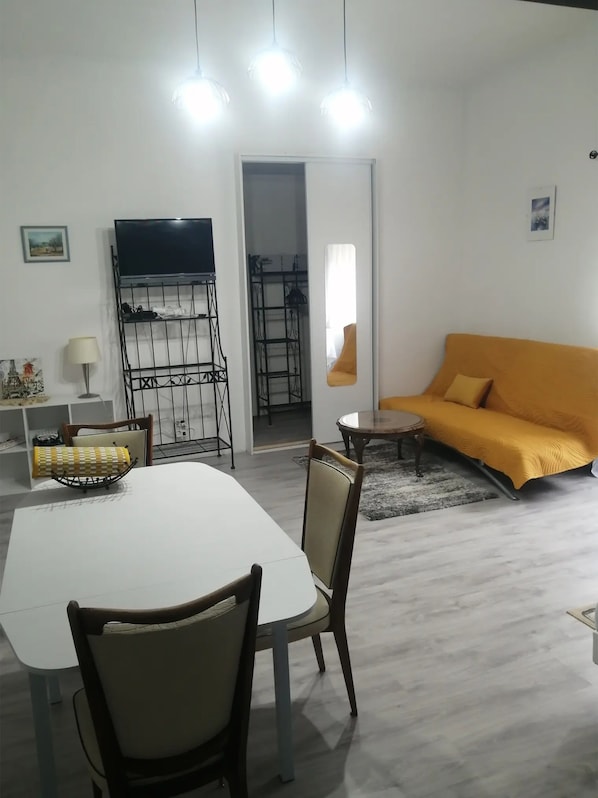 A living room with a white table, chairs, a sofa, a TV, and a metal rack.
