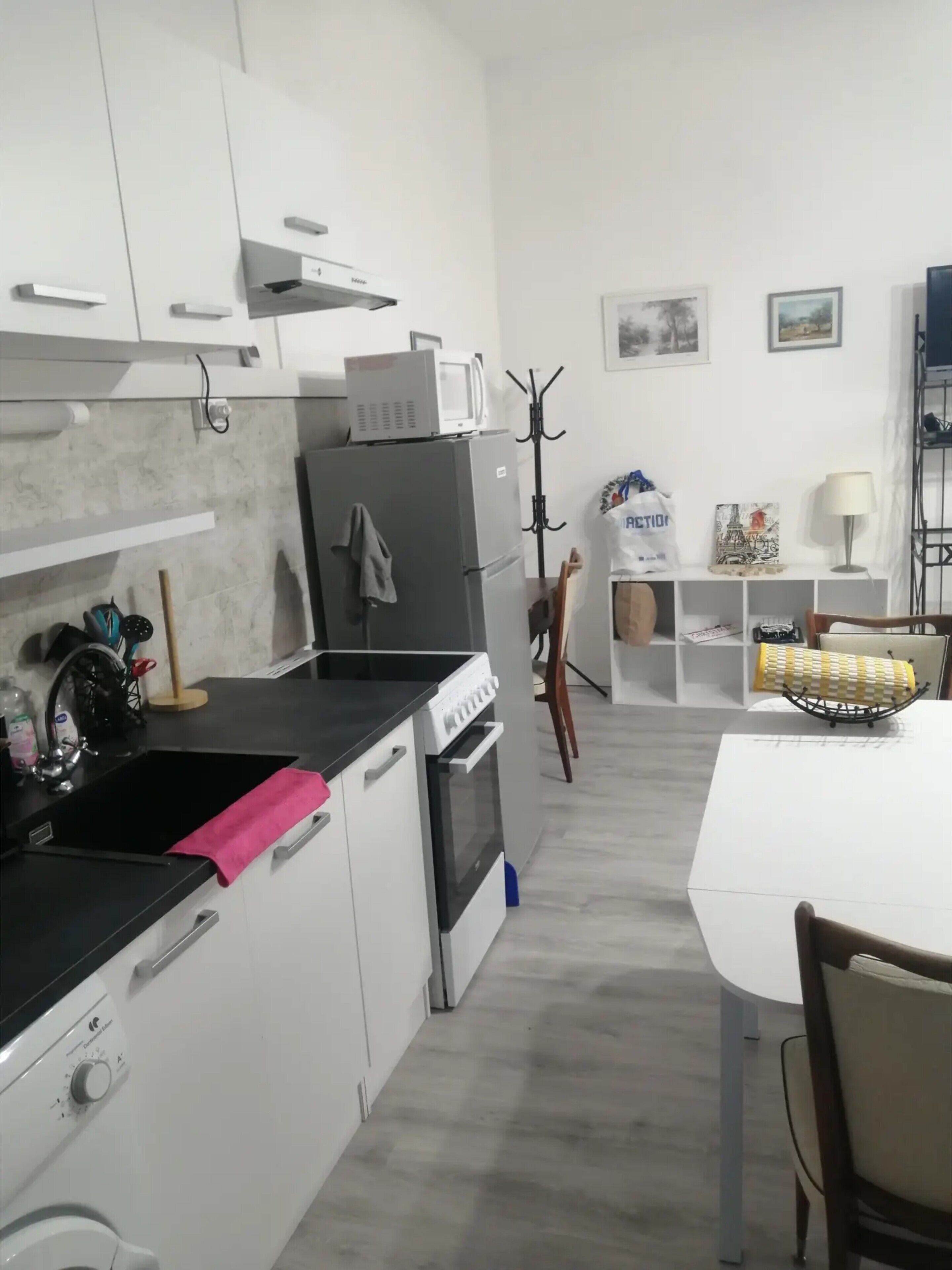 Een moderne keuken met witte kasten, een zwart aanrecht, een inbouwoven en een magnetron. Er is een zithoek met een witte tafel en stoelen.