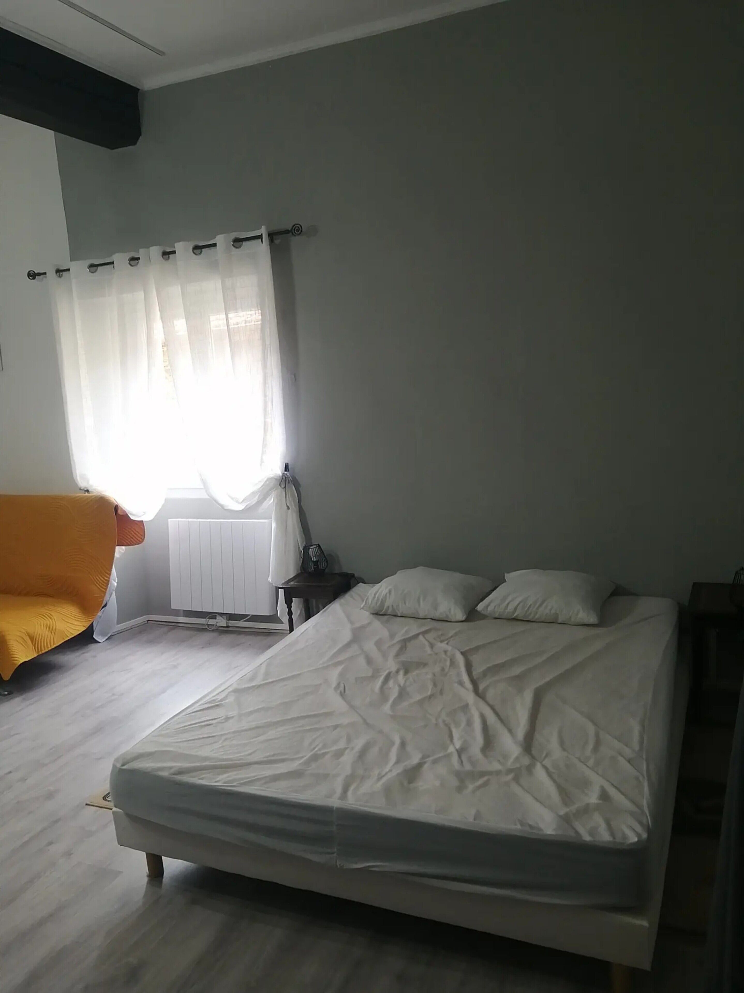Un dormitorio con cama, una silla, un radiador y una ventana con cortinas.