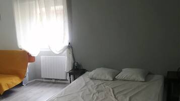 Un dormitorio con cama, una silla, un radiador y una ventana con cortinas.