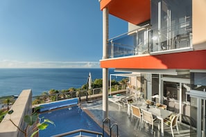 A poolside area with a view of the ocean, outdoor seating, and a glass-enclosed balcony.