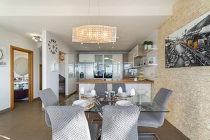 A modern kitchen with a central island, a dining area with a glass table and patterned chairs, and a large painting on the wall.