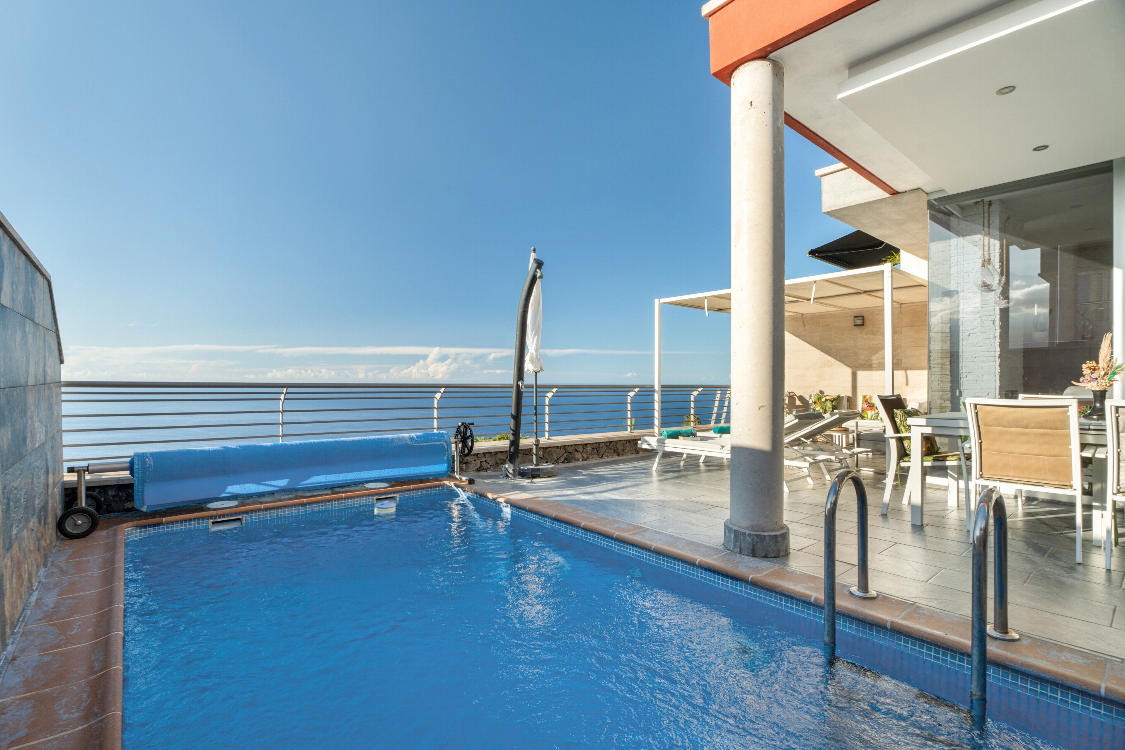 A pool area with a view of the sea, a covered seating area, and a poolside bar.