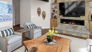 Ein modernes Wohnzimmer mit Kamin aus Stein, einem Flachbildfernseher und einem Couchtisch aus Holz.