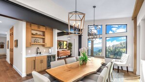 Eine moderne Küche mit Holzausbau, einem großen Esstisch und Blick ins Freie durch große Fenster.