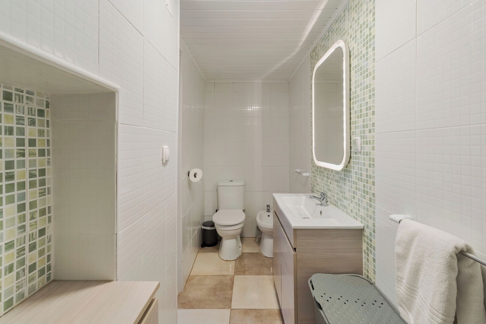 A bathroom with white tiled walls, a toilet, a sink, and a mirror.