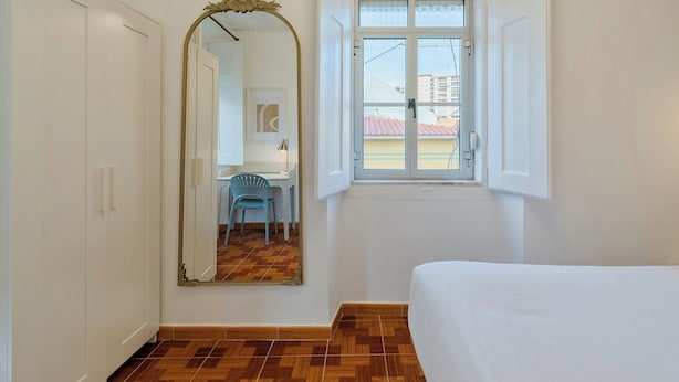 Een slaapkamer met een bed, een raam, een spiegel en een bureau met een stoel.