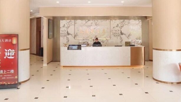 A hotel reception area with a marble wall, a reception desk, and a digital screen. - Traffic Hotel (Dabu)