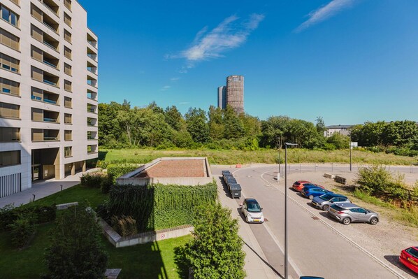 Un moderno edificio de apartamentos con un estacionamiento y una torre alta al fondo.