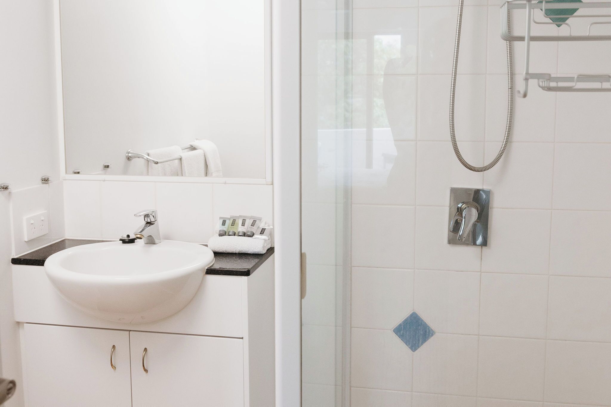 A bathroom with a white sink, a mirror, a shower with a glass door, and a towel rack.