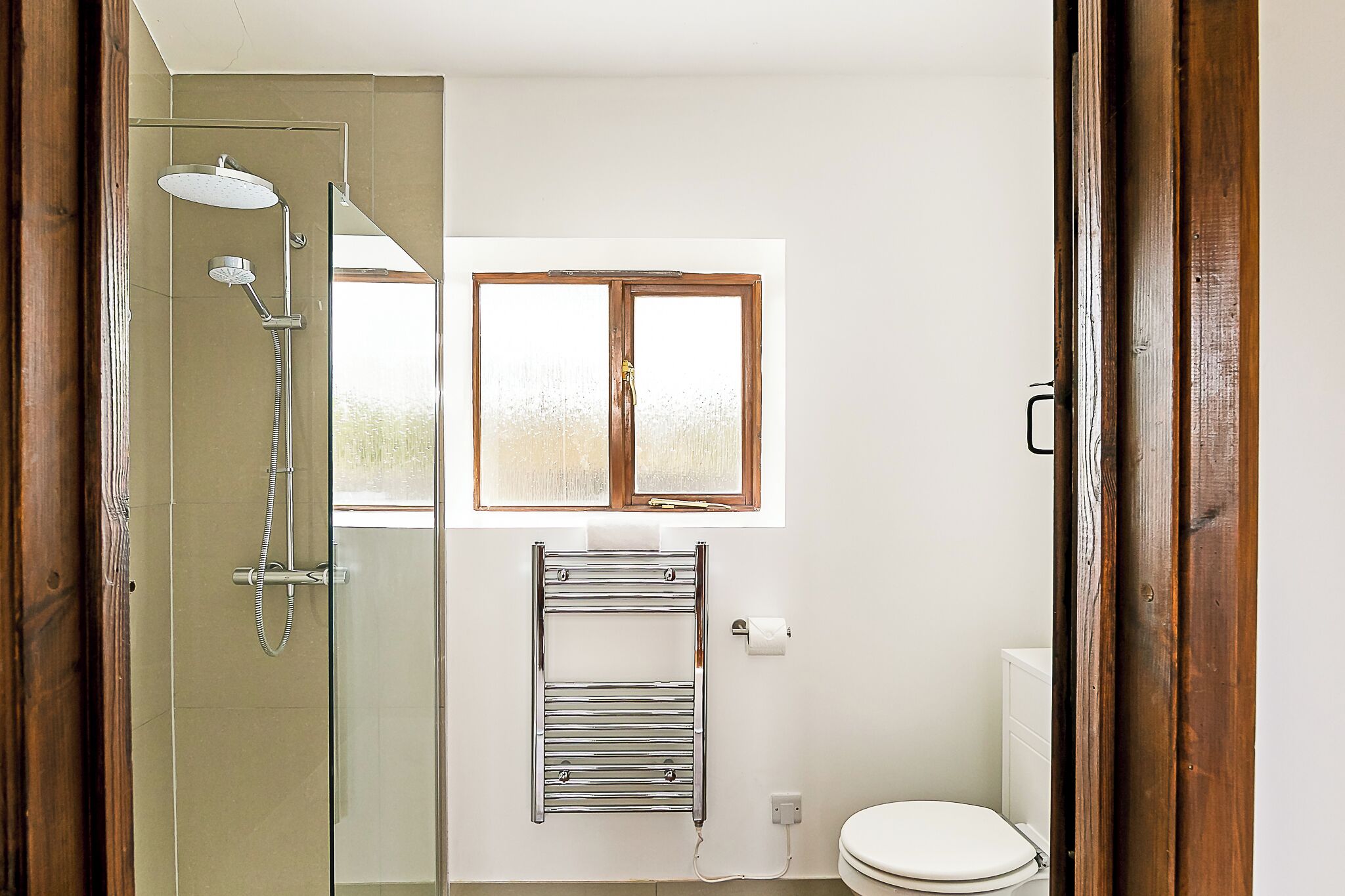 Une salle de bain avec une douche à parois de verre, un porte-serviettes, une fenêtre et des toilettes.
