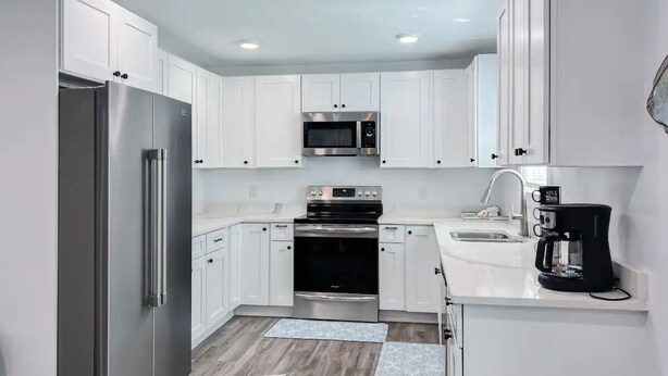 A modern kitchen with white cabinets, stainless steel appliances, and a black coffee maker. - Cozy Coastal Abode- 4bed,3bath (Brunswick)