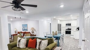 A modern living room with a green sofa, dining area, and kitchen. - Cozy Coastal Abode- 4bed,3bath (Brunswick)