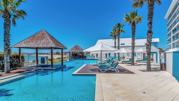 A pool area with lounge chairs, palm trees, and a gazebo. - Nautica Residences Mandurah (Mandurah)