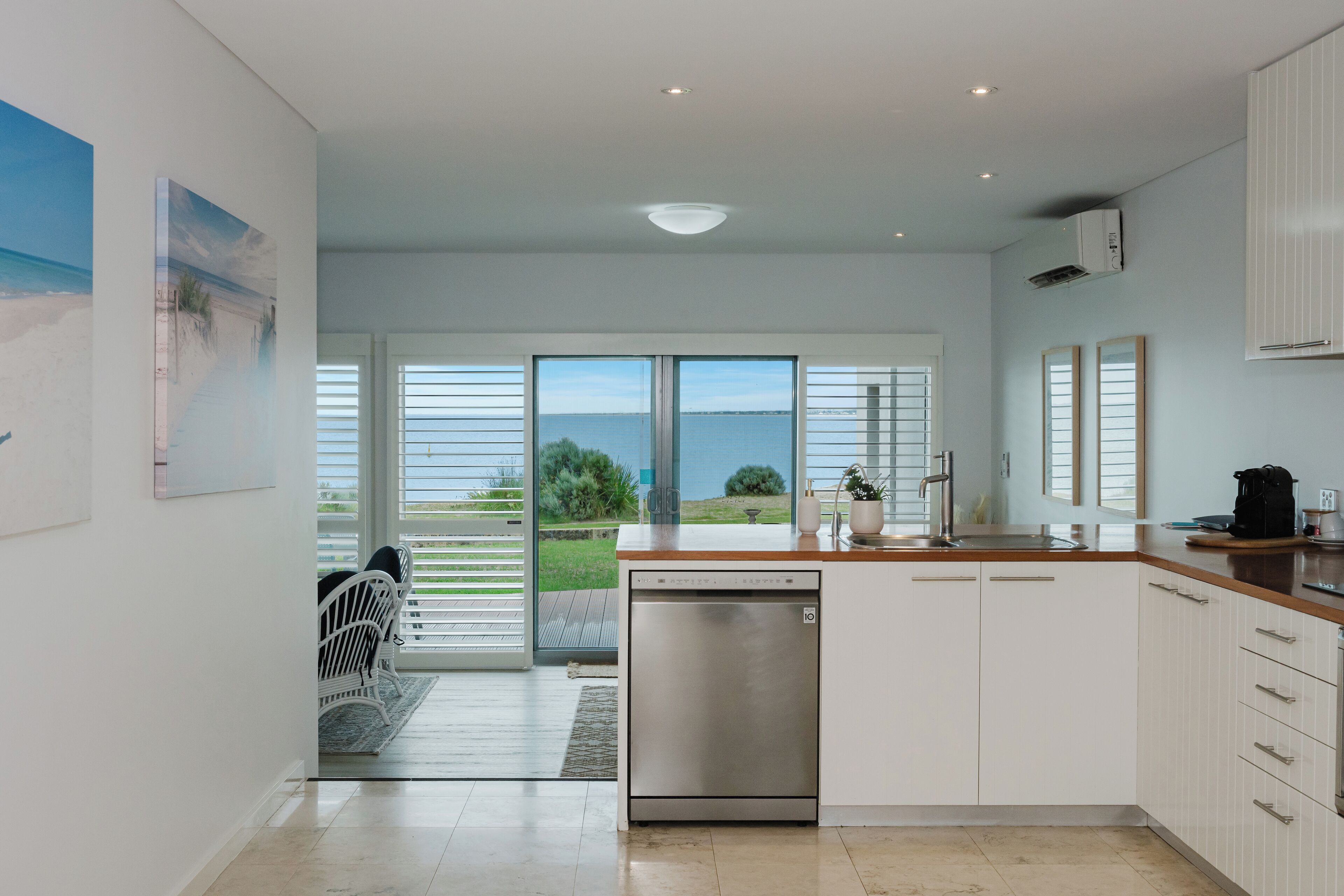 A modern kitchen with a dishwasher, white cabinets, and a view of the outdoors.