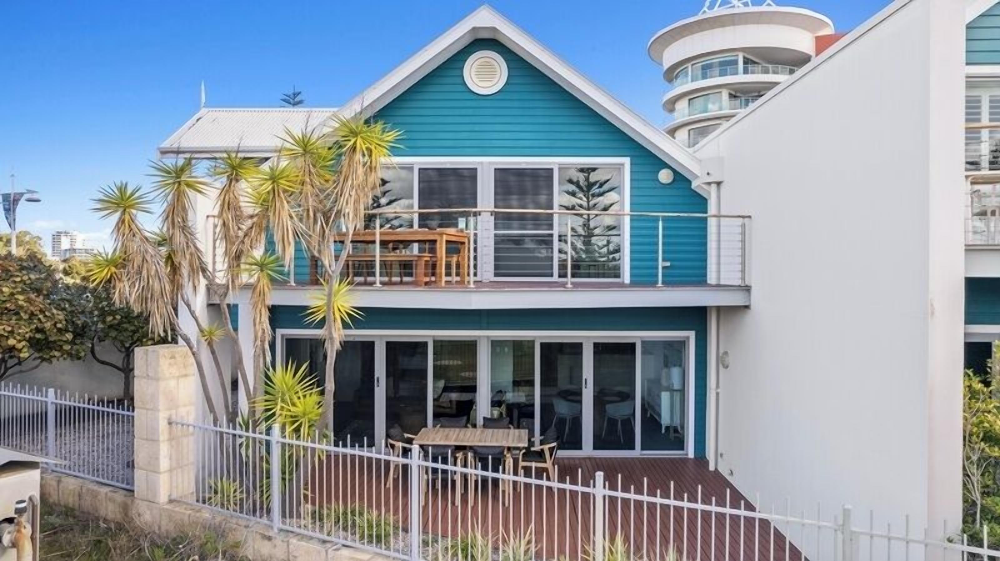 Una casa de dos pisos con balcón, ventanas amplias y patio cercado.
