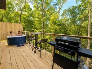 Een houten terras met een jacuzzi, een barbecue en buitenmeubels.