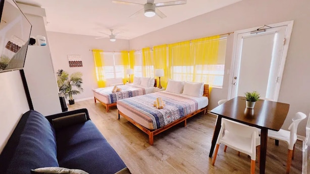 Ein modernes Zimmer mit zwei Betten, einer Schlafcouch, einem Esstisch und einem Deckenventilator.