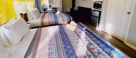 A hotel room with a bed, a desk, a chair, a TV, and a kitchenette.