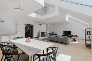 Relax in this open-plan living space with a high ceiling and skylight, featuring a dining area and cozy seating area with a flat-screen TV.