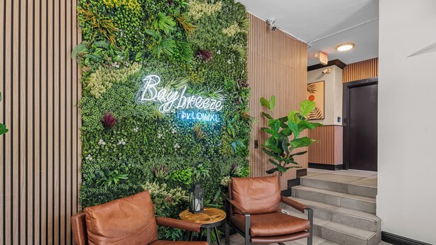 A lobby with a green wall, two brown leather chairs, a small wooden table, and a neon sign that reads "Bay Breeze Pillow Lounge". - Bright SoBe Corner Studio | Free Parking & Beach Perks | Prime Location (Miami Beach)