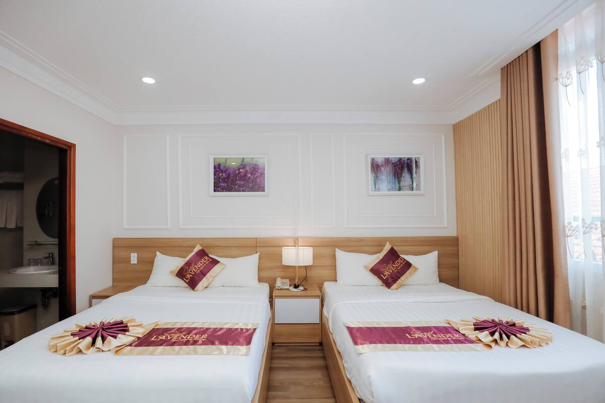 A hotel room with two beds, a wooden headboard, a nightstand with a lamp, and artwork on the walls.