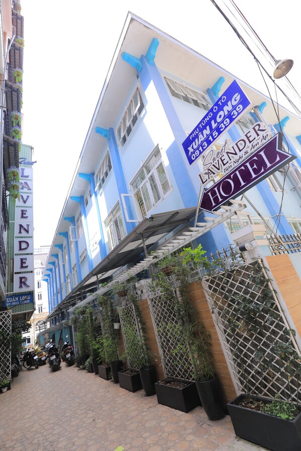 Un hotel con facciata blu e bianca, un cartello con la scritta 'PHU TUNG O TO YUAN LONG' e 'LAVENDER HOTEL', e una strada pavimentata con motociclette parcheggiate e piante in vaso.