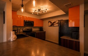 A kitchen with a large island, stainless steel appliances, and orange cabinetry.