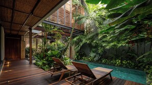 Eine Holzterrasse mit Liegestühlen und einem Pool, umgeben von üppiger tropischer Vegetation.