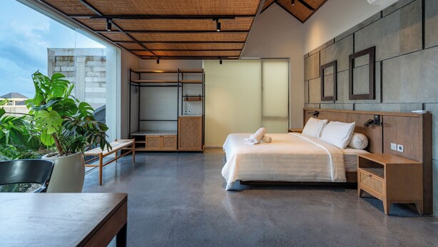 Ein modernes Schlafzimmer mit einem großen Bett, einem Nachttisch aus Holz, einer Topfpflanze und Blick auf die Stadt.