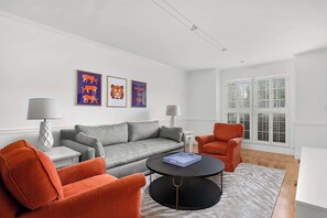A living room with a grey sofa, orange armchairs, a round coffee table, and framed tiger artwork on the wall.