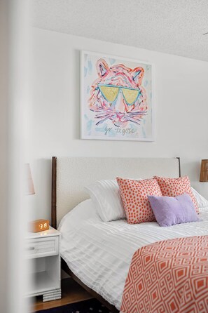 A neatly made bed with patterned bedding, a wall clock, and a colorful artwork above the bed.