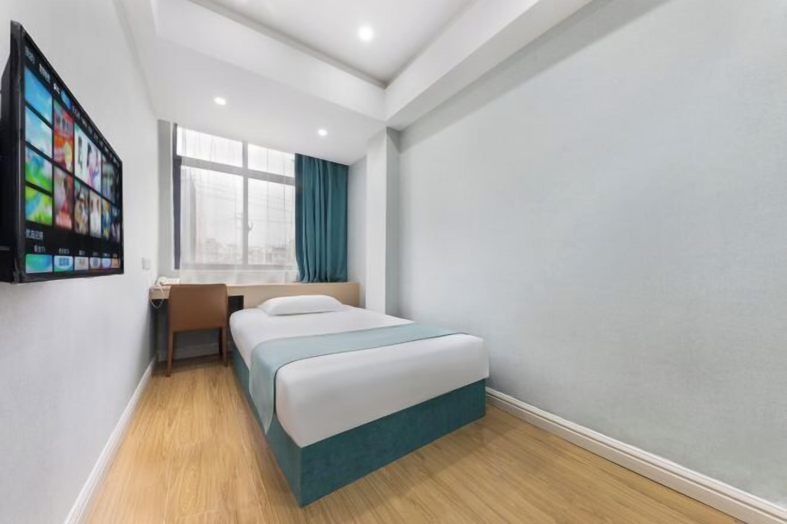 Habitación de hotel compacta con cama, escritorio, silla y ventana grande.