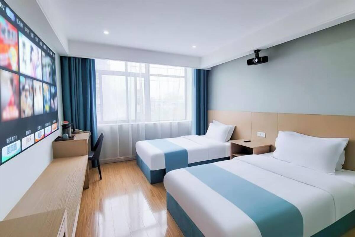 Une chambre d’hôtel avec deux lits, un bureau, un téléviseur fixé au mur et une fenêtre avec des rideaux.