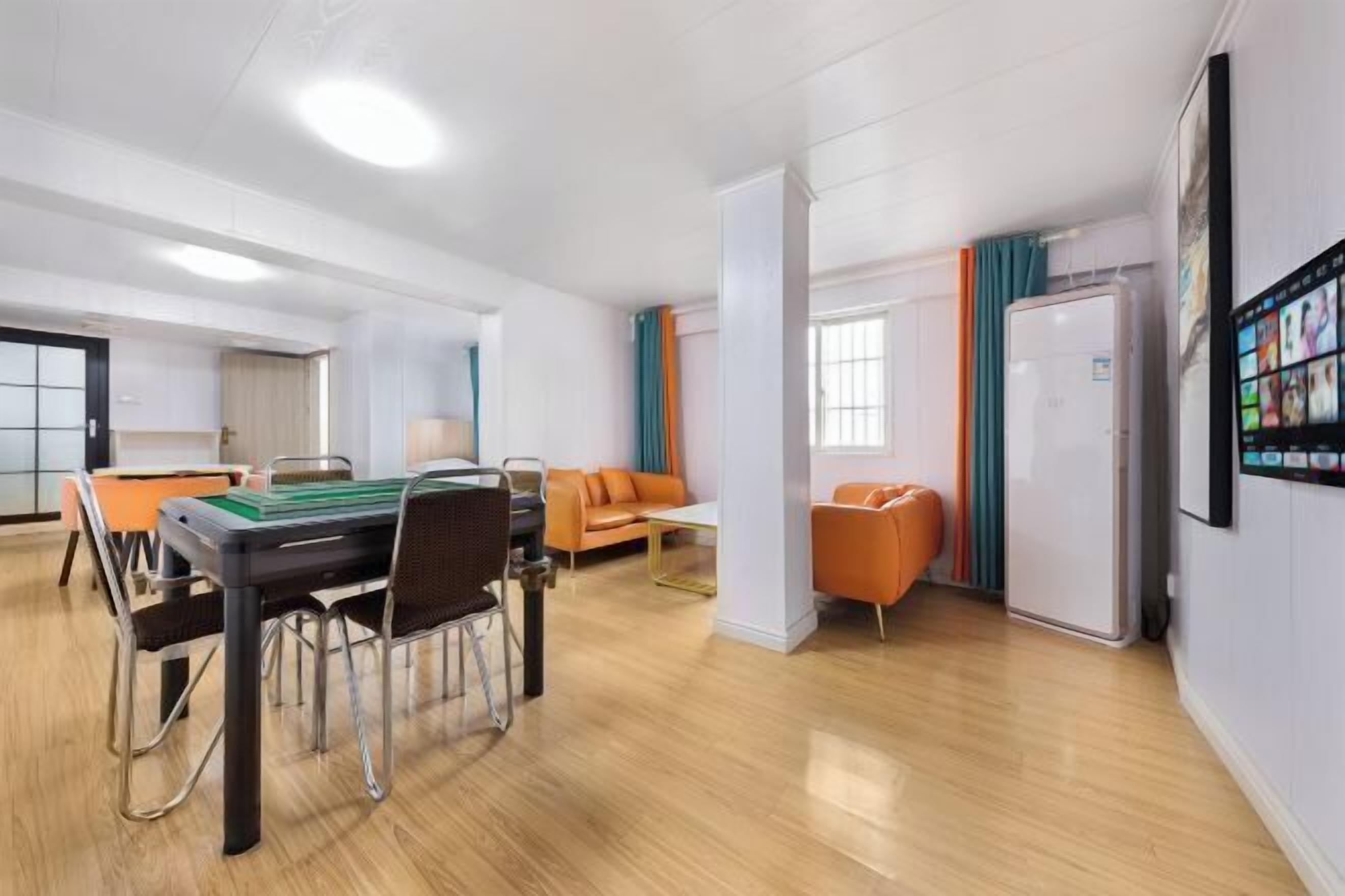 A modern hotel room with a dining area, a sofa, a television, and a refrigerator.