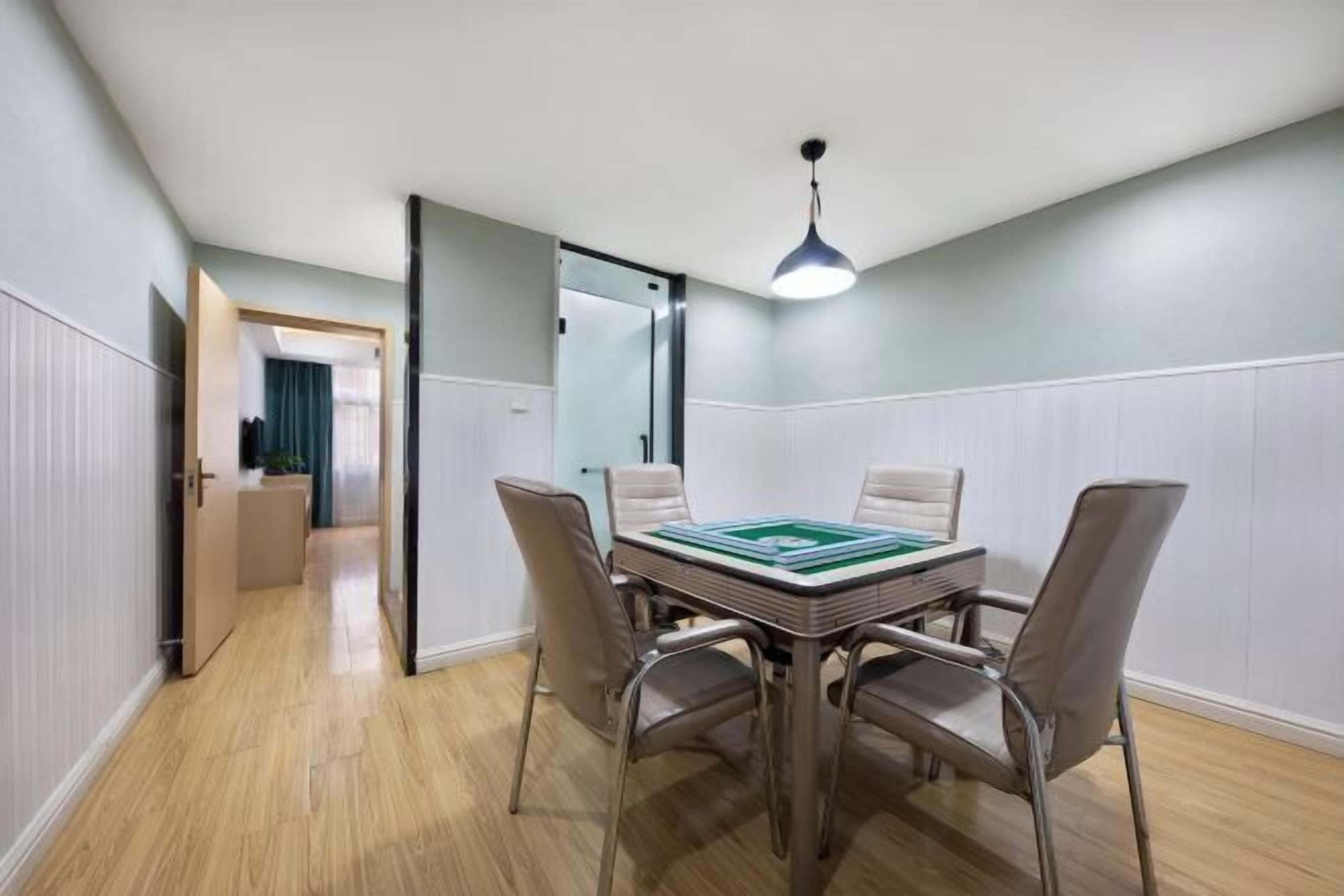 A room with a dining table, four chairs, a ceiling light, and a door leading to another room.