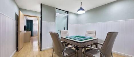 A room with a dining table, four chairs, a ceiling light, and a door leading to another room.