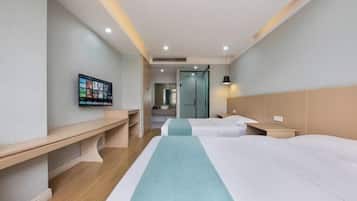 A hotel room with two beds, a desk, a TV mounted on the wall, and a bathroom visible through an open door.