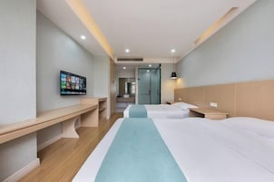Quarto de hotel com duas camas, uma escrivaninha, televisão na parede e um banheiro visível por uma porta aberta.
