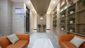 Um hall moderno com dois sofás de couro laranja, piso de mármore e um aparador com plantas em vasos.