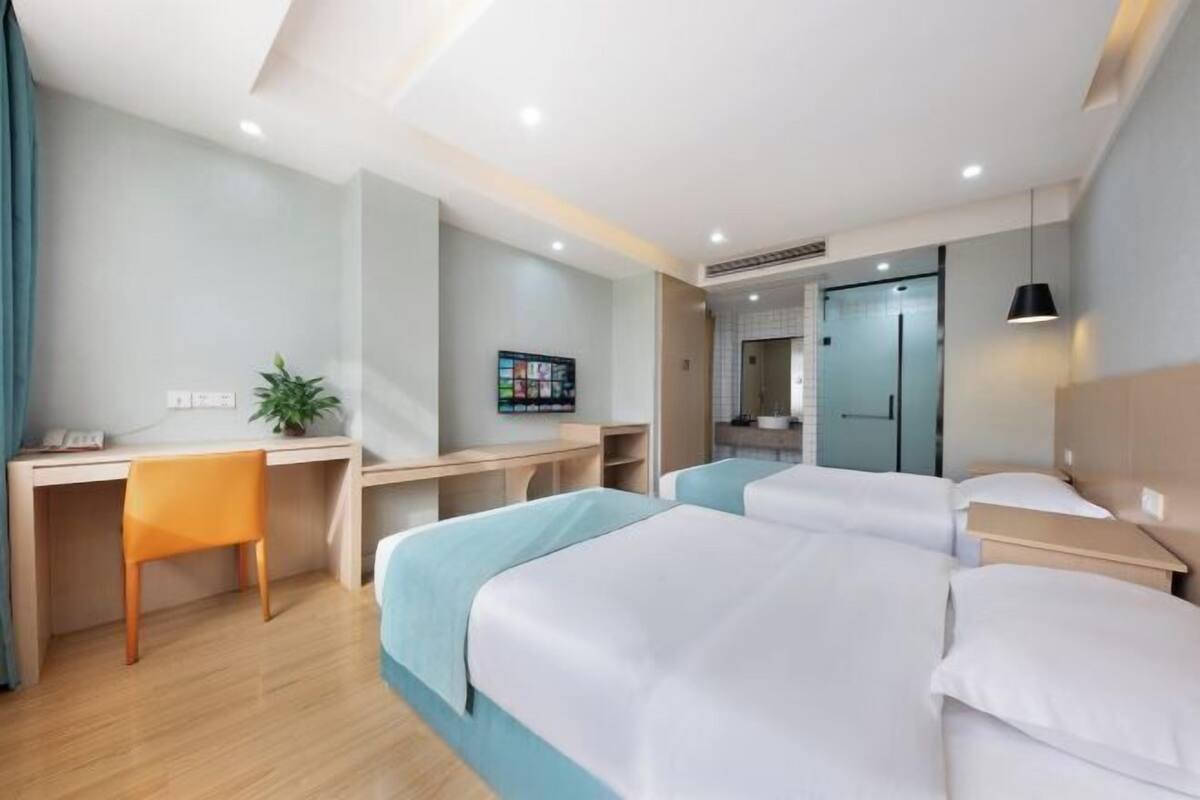 Une chambre d’hôtel avec deux lits, un bureau, une chaise, une télévision et une plante.