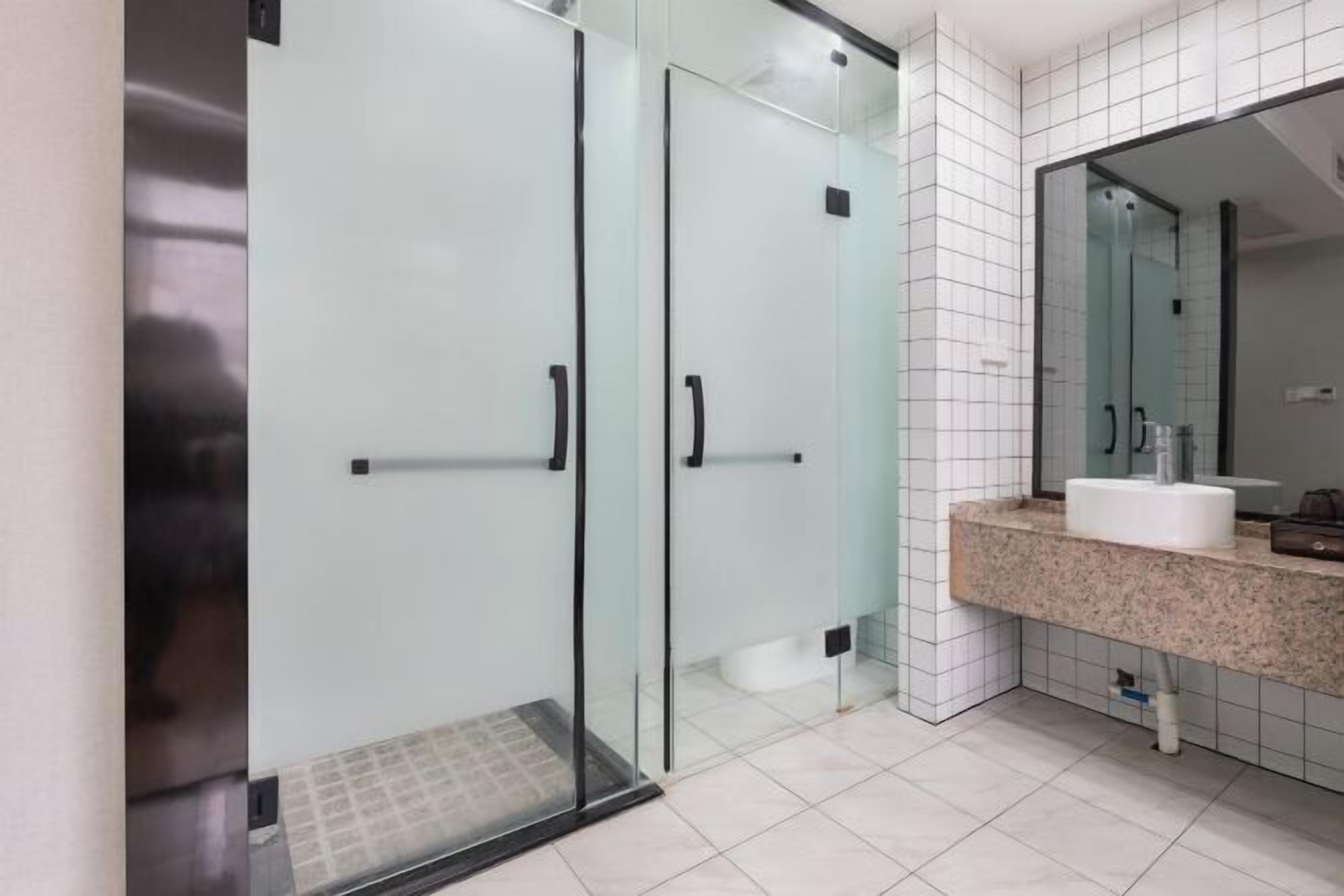 A modern bathroom with a glass shower enclosure, a white sink, and a large mirror.