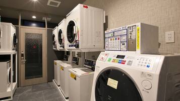 A laundry facility with multiple washing machines and dryers, a control panel, and a door with a security lock.