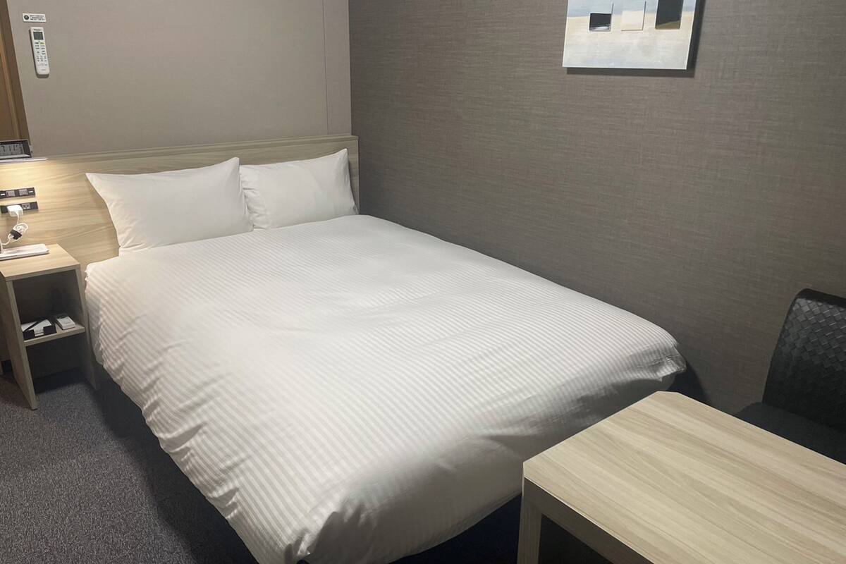 Habitación de hotel con una cama grande, una mesita de noche, un escritorio y un teléfono en la pared.
